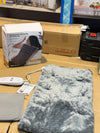 A massage heating pad with its packaging box in the background, placed on a wooden surface.