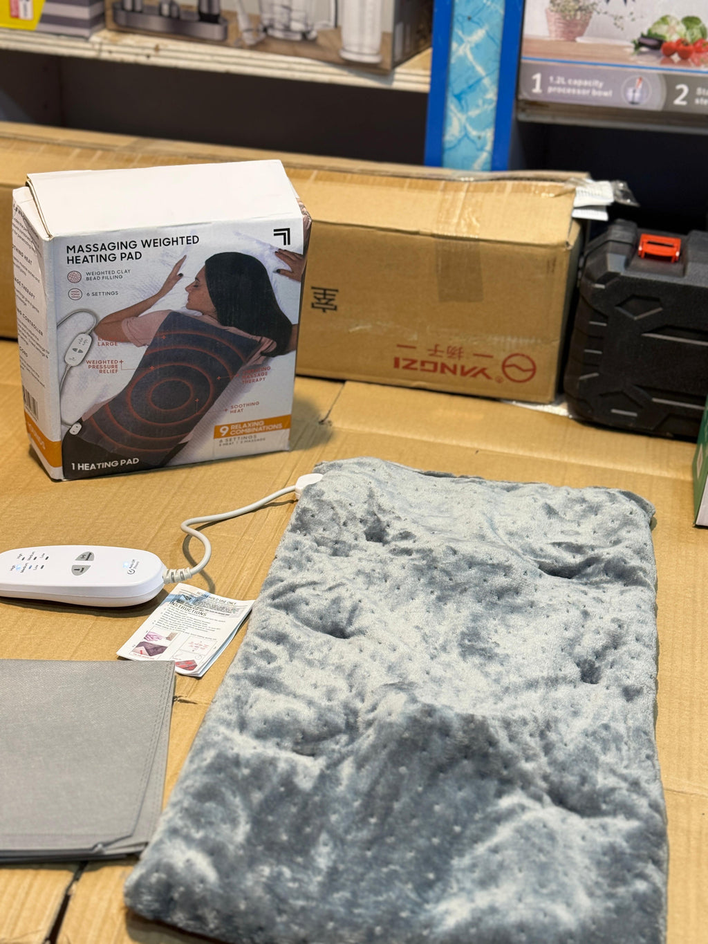 A massage heating pad with its packaging box in the background, placed on a wooden surface.